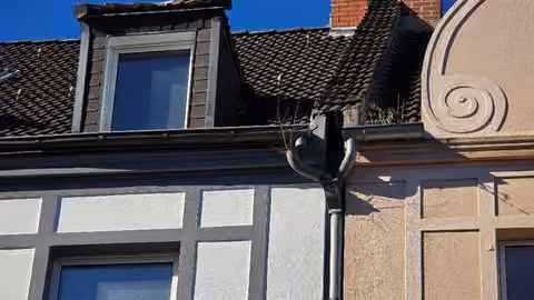 Zwangsversteigerung Eigentumswohnung in Gelsenkirchen, Rotthausen – Detailaufnahme der abgelösten Dachrinne mit Pflanzenbewuchs.