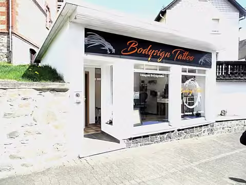 Zwangsversteigerung Grundstück in Gladenbach, Weidenhausen – Vorderansicht der Südseite des als Tattoostudio genutzten Kleingebäudes.
