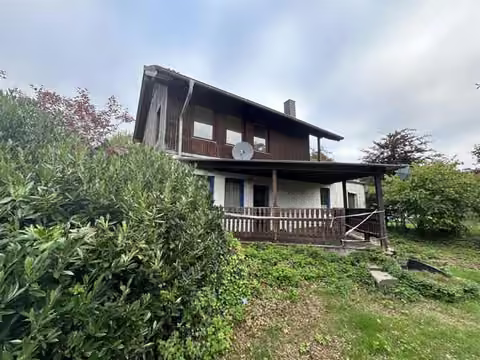 Zwangsversteigerung Eigentumswohnung in Hürtgenwald, Vossenack – Rückseite des ehemaligen Einfamilienhauses mit Holzlager auf der Terrasse.