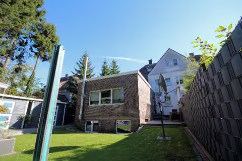 Zwangsversteigerung Eigentumswohnung in Marl, Brassert – Rückansicht des Gebäudes mit Gartenfläche und dem modernen Anbau.