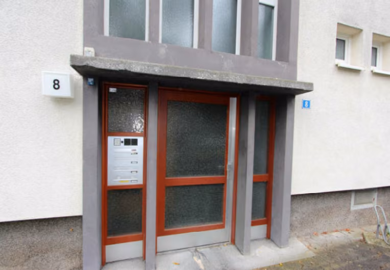 Zwangsversteigerung Eigentumswohnung in Köln, Gremberghoven – Seitenansicht des Wohngebäudes mit Grünfläche.