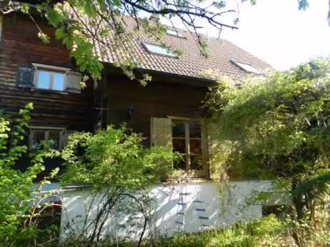 Zwangsversteigerung Einfamilienhaus in Seukendorf – Außenansicht Südfassade des Holzblockhauses mit Fenstern und Dachbereich.