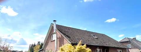 Zwangsversteigerung Einfamilienhaus in Metelen – Außenansicht des freistehenden Einfamilienhauses von Osten mit Vorgarten und Edelstahlschornstein.