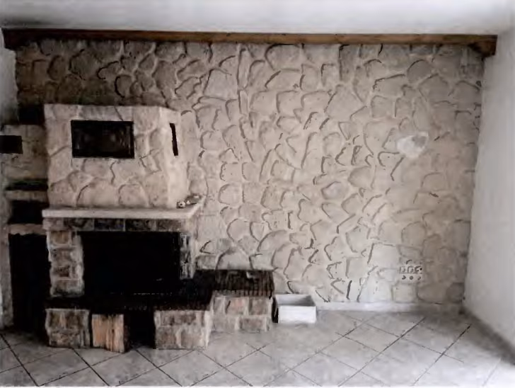Zwangsversteigerung Reihenhaus in Burgkirchen, Hirten – Wohnzimmerwand mit Steinbelag und stillgelegtem Kamin.