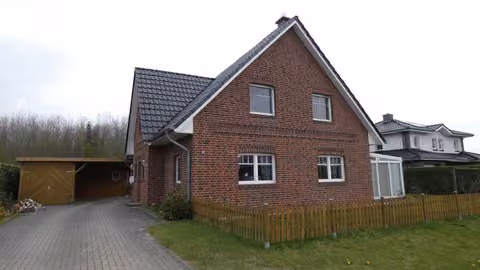 Zwangsversteigerung Einfamilienhaus in Barßel, Elisabethfehn – Front- und Seitenansicht des Einfamilienhauses mit Zufahrt und Vorgarten.