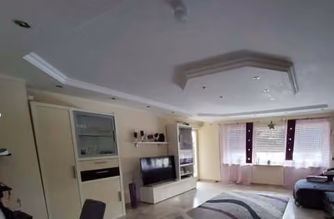Zwangsversteigerung Mehrfamilienhaus in Schwanfeld – Wohnzimmer im Erdgeschoss mit abgehängter Decke und Beleuchtung.
