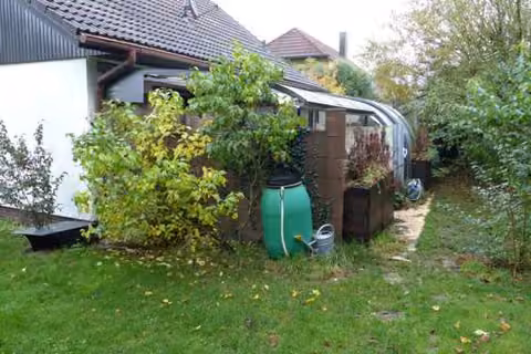 Zwangsversteigerung Einfamilienhaus in Langenzenn – Gartenansicht mit Terrasse und Wintergartenüberdachung.