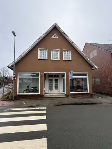 Zwangsversteigerung Einfamilienhaus in Quakenbrück – Giebelansicht Süd-West mit verputzter Erdgeschossfassade und Schaufensterfront.