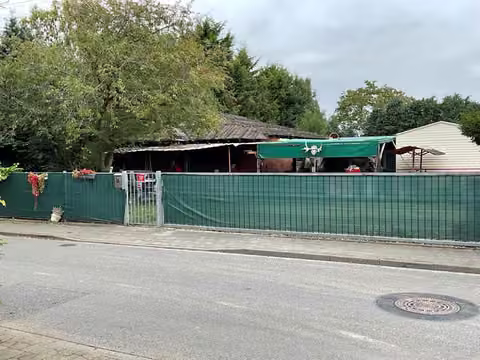 Zwangsversteigerung Einfamilienhaus in Selfkant, Hoengen – Straßenansicht des Grundstücks mit Umzäunung und Container-Wohnhaus.