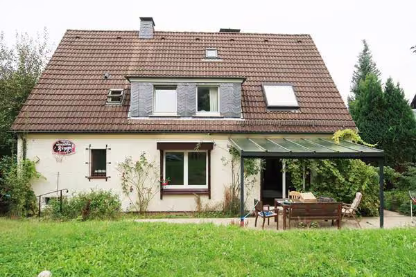 Zwangsversteigerung Einfamilienhaus in Schwelm – Rückwärtige Ansicht der Gartenseite mit überdachter Terrasse und Rasenfläche.