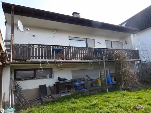 Zwangsversteigerung Einfamilienhaus in Mömbris, Daxberg – Rückwärtige Gebäudeansicht mit Balkon und Garten.