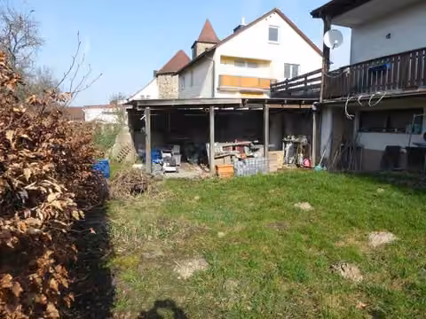 Zwangsversteigerung Einfamilienhaus in Mömbris, Daxberg – Gartenansicht mit überdachtem Lagerbereich und Grünfläche.