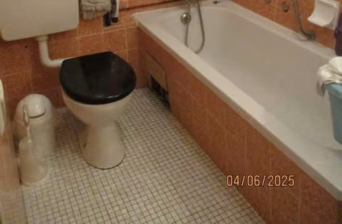 Zwangsversteigerung Eigentumswohnung in Nienburg/Weser – Innenansicht des gefliesten Badezimmers mit Badewanne und WC.