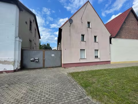 Zwangsversteigerung Einfamilienhaus in Südliches Anhalt, Reupzig – Straßenansicht des Vorderhauses mit Hoftor und angrenzendem Anbau.