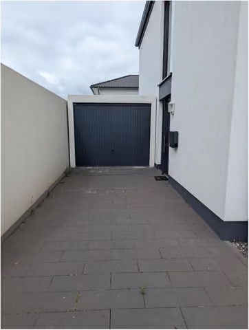 Zwangsversteigerung Einfamilienhaus in Zülpich, Wichterich – Gepflasterte Zufahrt zur Fertiggarage mit anthrazitfarbenem Tor.