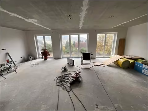 Zwangsversteigerung Einfamilienhaus in Nußbach – Wohnzimmer im Erdgeschoss mit bodentiefen Fenstern im Rohbauzustand.