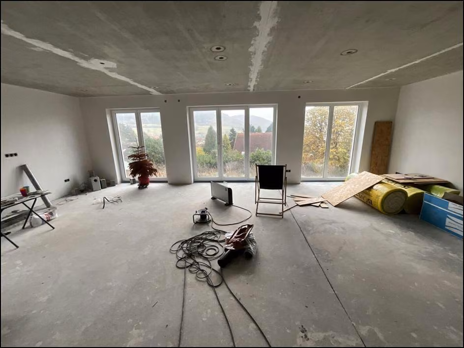 Zwangsversteigerung Einfamilienhaus in Nußbach – Wohnzimmer im Erdgeschoss mit bodentiefen Fenstern im Rohbauzustand.