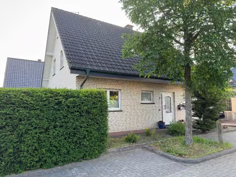 Zwangsversteigerung Einfamilienhaus in Rheine, Dutum – Seitenansicht mit Hecke und gepflasterter Zufahrt.