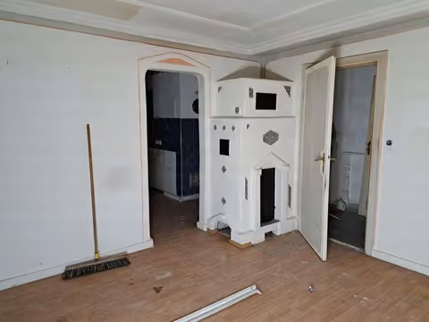 Zwangsversteigerung Doppelhaushälfte in Obergeislbach – Wohn- und Schlafzimmer im Erdgeschoss mit Kachelofen.