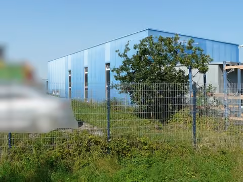 Zwangsversteigerung Grundstück in Geseke – Seitenansicht der Produktionshalle von Osten über die Einfriedung.