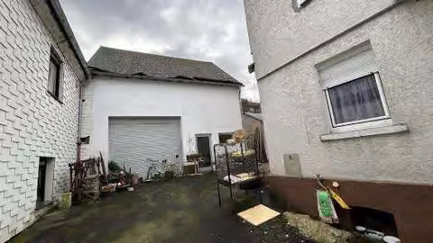 Zwangsversteigerung Einfamilienhaus in Eschenburg, Simmersbach – Außenansicht des Nebengebäudes mit Rolltor und Hoffläche.