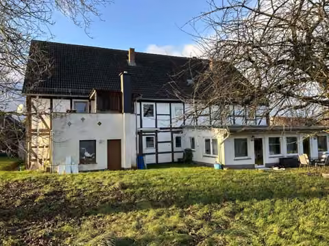 Zwangsversteigerung Mehrfamilienhaus in Einbeck, Holtensen – Rückansicht des Gebäudes von Südosten mit Garten und Sichtfachwerk.