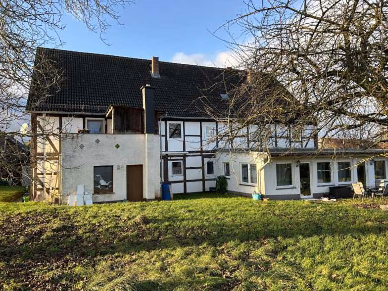 Zwangsversteigerung Mehrfamilienhaus in Einbeck, Holtensen – Rückansicht des Gebäudes von Südosten mit Garten und Sichtfachwerk.