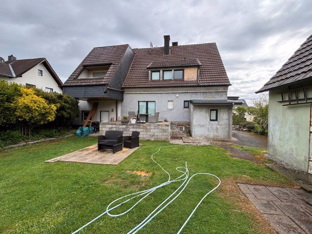 Zwangsversteigerung Zweifamilienhaus in Neuenrade, Küntrop – Gartenseitige Ansicht des Wohnhauses mit Terrasse und Anbauten.