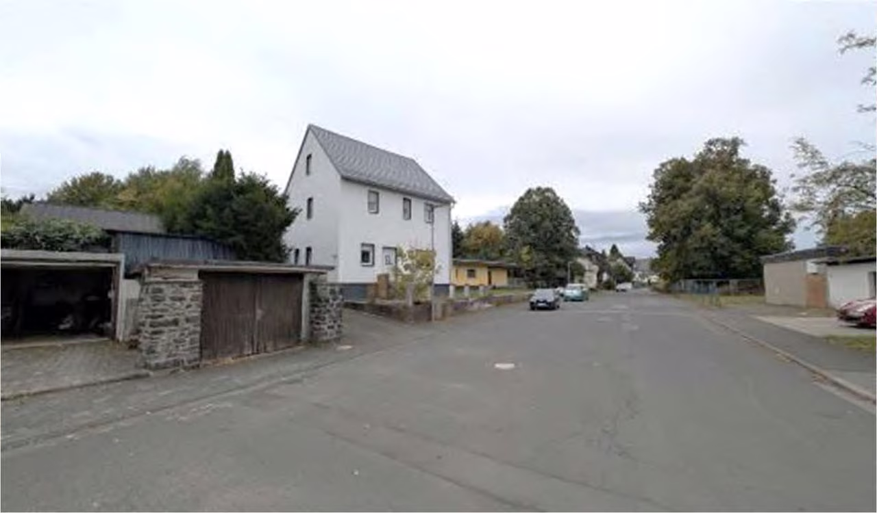 Zwangsversteigerung Eigentumswohnung in Driedorf – Straßenansicht mit Zufahrt und Nebengebäuden.