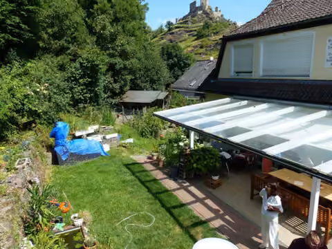 Zwangsversteigerung Zweifamilienhaus in Kobern-Gondorf, Kobern – Rückansicht des Hauptwohnhauses mit überdachter Terrasse und Hanglage.