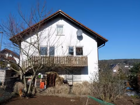 Zwangsversteigerung Einfamilienhaus in Ebersburg, Schmalnau – Blick vom Garten auf die südöstliche Giebelseite des Wohngebäudes mit Balkon.