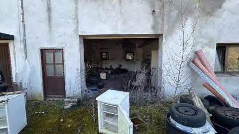 Zwangsversteigerung Zweifamilienhaus in Waldsolms, Hasselborn – Garagengebäude mit offener Einfahrt und Gerümpel im Außenbereich.