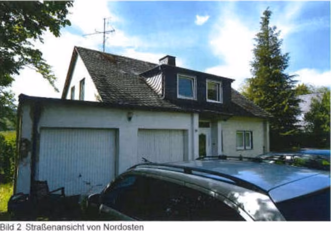 Zwangsversteigerung Mehrfamilienhaus in Brilon, Gudenhagen / Petersborn – Straßenansicht von Nordosten mit Zufahrt und den beiden integrierten Garagen.