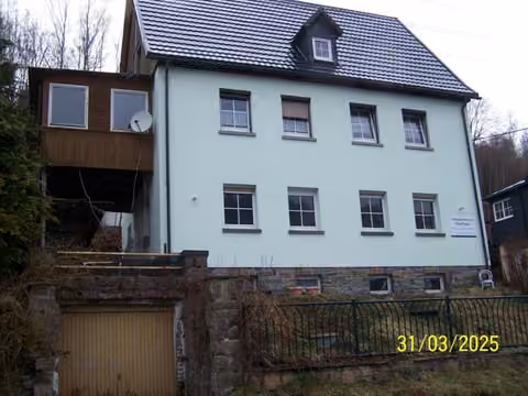 Zwangsversteigerung Einfamilienhaus in Klingenthal, Brunndöbra – Vorderansicht des Einfamilienhauses mit Hanggarage und Wintergartenanbau.