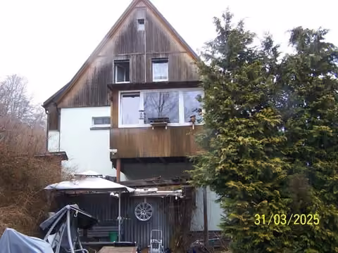 Zwangsversteigerung Einfamilienhaus in Klingenthal, Brunndöbra – Giebelansicht mit Wintergarten und terrassiertem Grundstücksbereich.