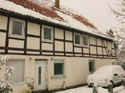 Zwangsversteigerung Zweifamilienhaus in Bad Driburg, Reelsen – Westseite mit Haupteingang und sichtbaren Feuchteschäden am Sockelputz.