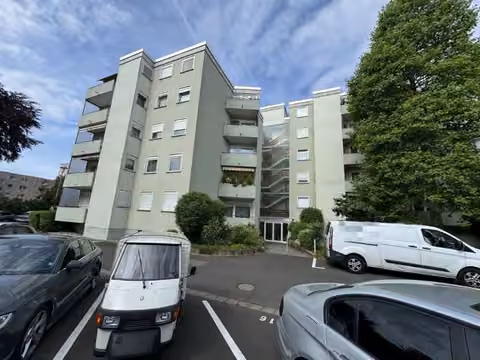 Zwangsversteigerung Eigentumswohnung in Maintal, Bischofsheim – Fassadenansicht des Gebäudes mit Eingangsbereich und davorliegendem Parkplatz.