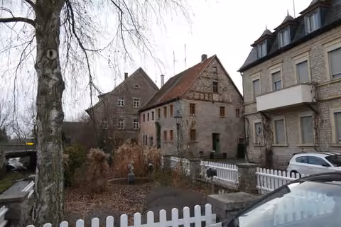 Zwangsversteigerung Einfamilienhaus in Dettelbach – Straßenansicht des Wohnhauses Am Rosengarten 6 mit Sichtmauerwerk und Fachwerkgiebel.