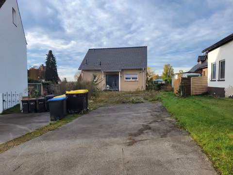 Zwangsversteigerung Einfamilienhaus in Hüllhorst, Oberbauerschaft – Ostansicht des Hauses mit gepflasterter Zufahrt und Nachbarbebauung.