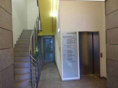Zwangsversteigerung Wohn-/Geschäftshaus in Bochum, Wattenscheid – Eingangsbereich und Treppenhaus mit Terrazzoboden und Personenaufzug.