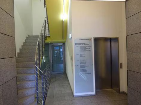 Zwangsversteigerung Wohn-/Geschäftshaus in Bochum, Wattenscheid – Eingangsbereich und Treppenhaus mit Terrazzoboden und Personenaufzug.