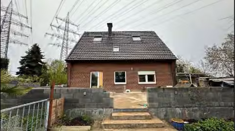 Zwangsversteigerung Einfamilienhaus in Wesel, Obrighoven – Süd-West-Ansicht mit sichtbaren Masten der Hochspannungsfreileitungen.