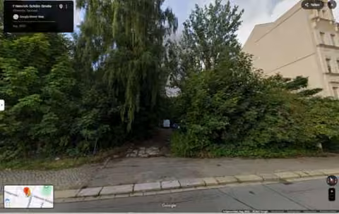 Zwangsversteigerung Grundstück in Chemnitz, Sonnenberg – Straßenansicht der Baulücke mit Baum- und Strauchbewuchs an der Heinrich-Schütz-Straße.