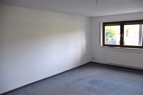 Zwangsversteigerung Eigentumswohnung in Werdau, Steinpleis – Wohnzimmer der Eigentumswohnung mit Raufasertapete und Heizkörper.