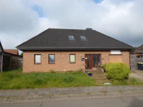 Zwangsversteigerung Einfamilienhaus in Heide, Süderholm – Schrägansicht des Gebäudes mit Garten- und Rasenfläche.