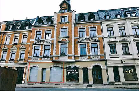 Zwangsversteigerung Büro in Oelsnitz – Straßenansicht des Gebäudes mit Schaufensterfront der Gewerbeeinheit im Erdgeschoss.