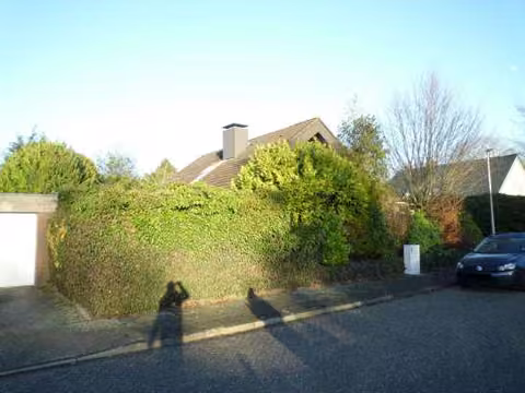 Zwangsversteigerung Einfamilienhaus in Nordhorn – Front- und Seitenansicht links mit bewachsener Grundstücksgrenze.
