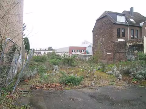Zwangsversteigerung Mehrfamilienhaus in Düsseldorf, Heerdt – Ansicht des unbebauten Baugrundstücks mit Wildwuchs und Nachbarbebauung
