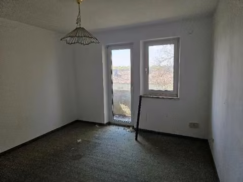 Zwangsversteigerung Eigentumswohnung in Augsburg, Hochzoll – Zimmer mit Balkontür und renovierungsbedürftigem Wand- und Bodenbelag.