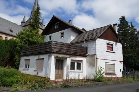 Zwangsversteigerung Einfamilienhaus in Münchhausen, Niederasphe – Südwestansicht des Einfamilienhauses mit Anbauten und Straßenverlauf.